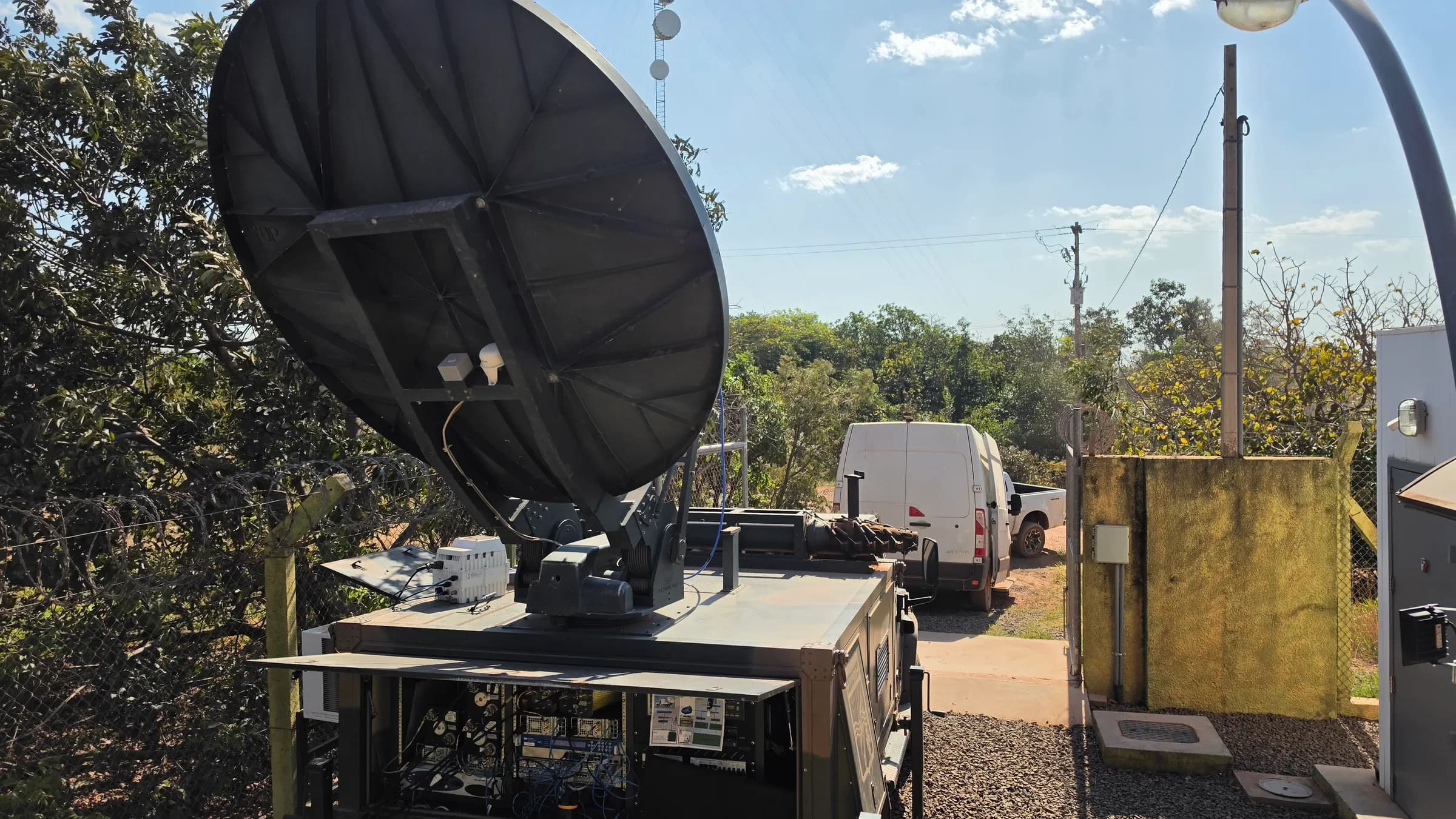Antena SATCOM instalada sobre abrigo tecnico em area remota, com veiculo da equipe da i3F ao fundo